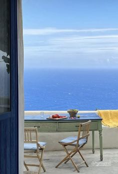 a table with two chairs sitting on top of it next to an open window overlooking the ocean