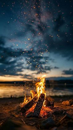 a campfire is lit up at night on the beach with stars in the sky