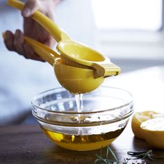 a person pouring olive oil into a bowl with lemons on the table next to it