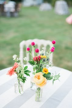 two vases filled with flowers sitting on top of a white tablecloth covered table