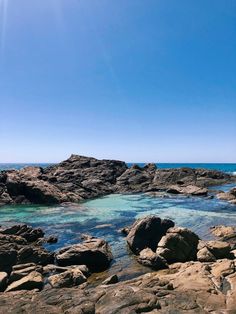 the water is crystal blue and clear on this rocky beach area with large rocks in the foreground