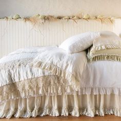 a white bed with ruffled bedspread and pillows on it's headboard