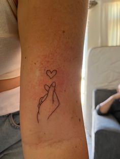 a woman with a tattoo on her arm holding a small heart in one hand and a finger in the other