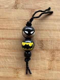 a black and yellow bead with a batman face on it's head is sitting on a wooden surface