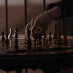 a person is playing chess on a table with other pieces in the foreground and one hand reaching for it