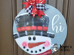 a door hanger with a snowman painted on it's face and red bow