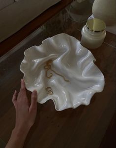 a person holding a ring dish on top of a wooden table next to a lamp