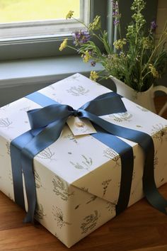 a wrapped gift box sitting on top of a wooden floor next to a vase with flowers