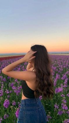 a woman standing in a field of flowers looking into the distance with her hand on her head