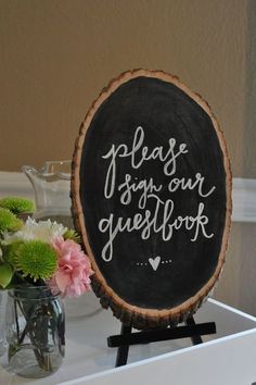 a wooden sign that says please sign our guestbook on it next to some flowers