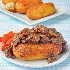 two plates with meat and vegetables on them, next to some breaded potato wedges