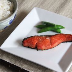 a white plate topped with fish and rice next to a bowl filled with green beans