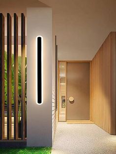 the entrance to a modern home with grass and lights on it's side wall