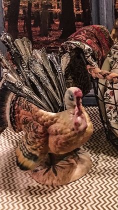 a statue of a turkey with feathers on it's head sitting in front of a painting