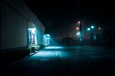 an empty street at night with the lights on and no cars parked in front of it