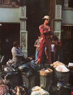 a woman standing in front of a pile of trash on the street next to other people