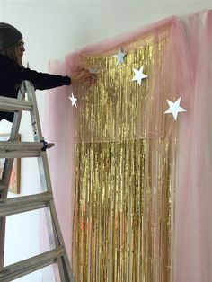 a woman standing on a ladder in front of a curtain with stars hanging from it