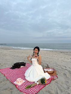 a woman sitting on top of a red and white checkered blanket at the beach