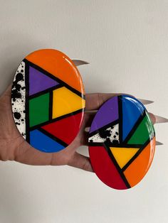 a hand holding two colorful buttons on top of each other in front of a white wall