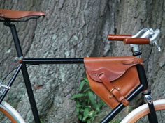 a bicycle with a leather saddle on the handlebars is parked next to a tree