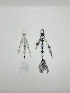 two key chains with charms attached to them on a white surface, one has a cross and the other is a leaf