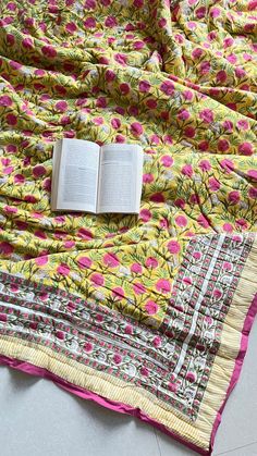 an open book laying on top of a quilted bedspread with pink and yellow flowers