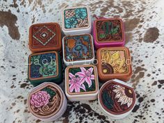 several tins with designs on them sitting on a cowhide surface in the shape of flowers