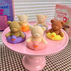 there are five small teddy bears sitting on a pink cake plate with a book in the background