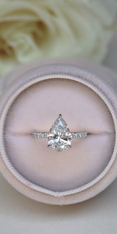 an engagement ring in a pink velvet box with white flowers behind it and a rose on the other side