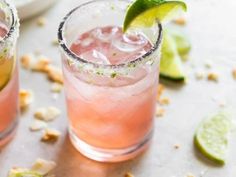 two glasses filled with pink and green cocktails next to lime slices on a table