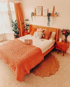 a bed with an orange bedspread in a bedroom next to a large window