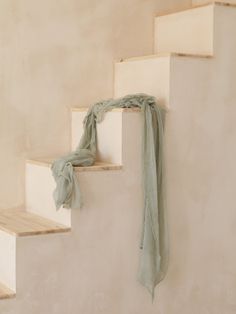 a green scarf hanging on the side of a set of stairs with white walls and wooden steps