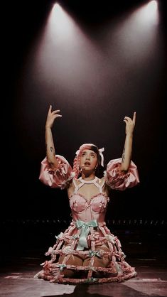 a woman in a pink dress sitting on top of a stage with her hands up