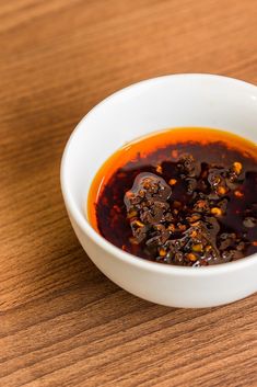 a small white bowl filled with sauce on top of a wooden table next to a spoon