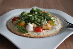 a small pizza on a white plate topped with vegetables