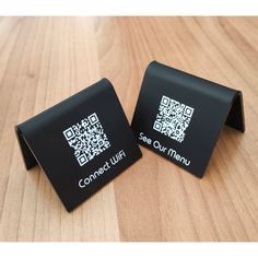 two black coasters with qr - code on them sitting on a wooden table