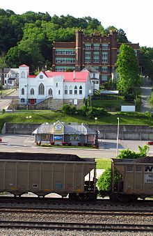 two train cars are on the tracks in front of a large white building with a red roof