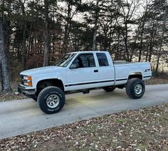 a white pick up truck parked on the side of a road in front of some trees