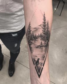 a person with a tattoo on their arm that has a lake and trees in it