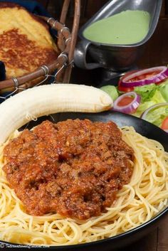 a plate of spaghetti with meat sauce and a banana on the table next to bread