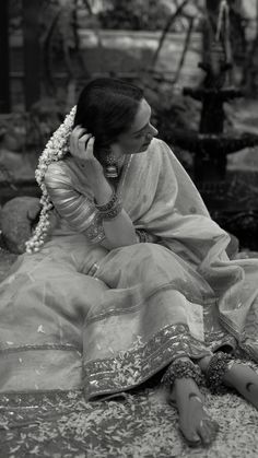 a woman sitting on the ground talking on a cell phone while wearing a sari