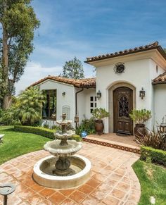 a house with a fountain in front of it and landscaping around the entrance to the home