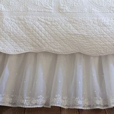 a white bedspread on top of a wooden floor next to a bed skirt