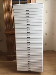 a tall white cabinet sitting on top of a hard wood floor next to a wall