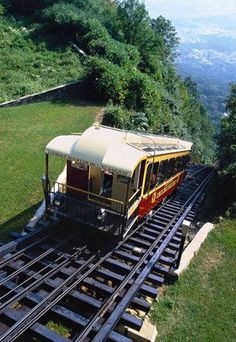 an aerial view of a train traveling down the tracks near a grassy area with trees and mountains in the background