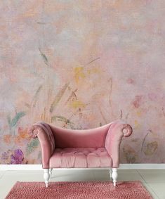 a pink chair sitting in front of a wall with flowers on it and a rug