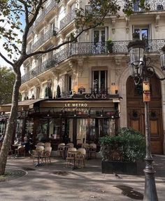 an old building with tables and chairs on the street in front of it, next to a lamp post