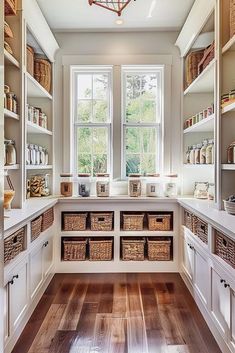 a kitchen filled with lots of white cupboards and wooden floors next to a window