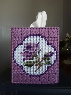 a tissue dispenser on top of a blue book with a purple rose