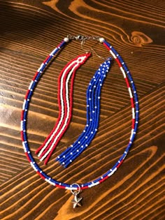 a red, white and blue beaded necklace on top of a wooden table with an american flag charm